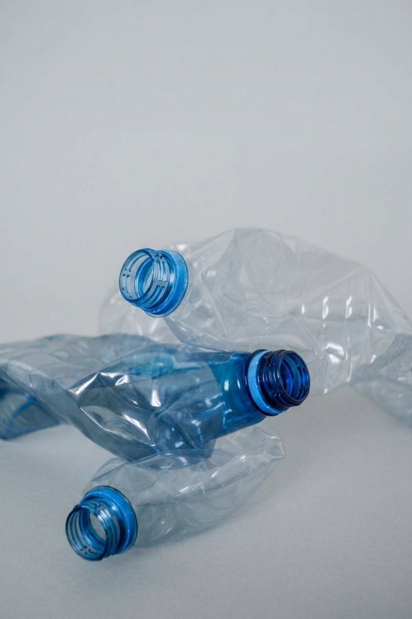 Three crushed blue plastic drinks bottles on a pale grey surface.