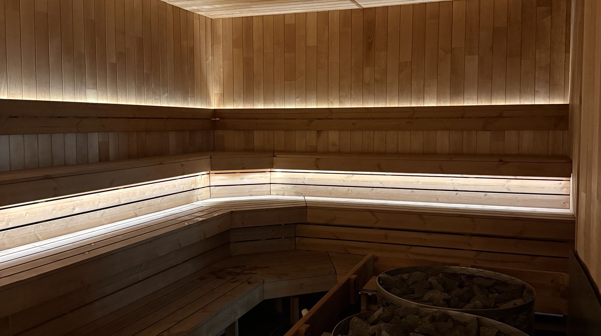 A sauna with pale timber benches and a heater, softly lit.